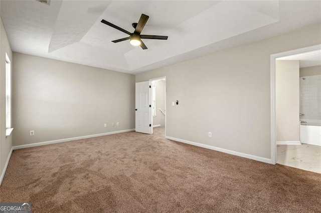 unfurnished bedroom featuring ceiling fan, baseboards, a tray ceiling, carpet, and ensuite bath