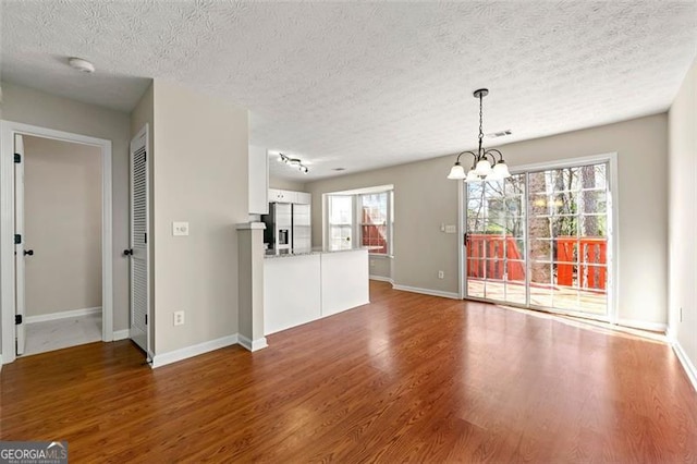 unfurnished living room with baseboards, a textured ceiling, a chandelier, and wood finished floors