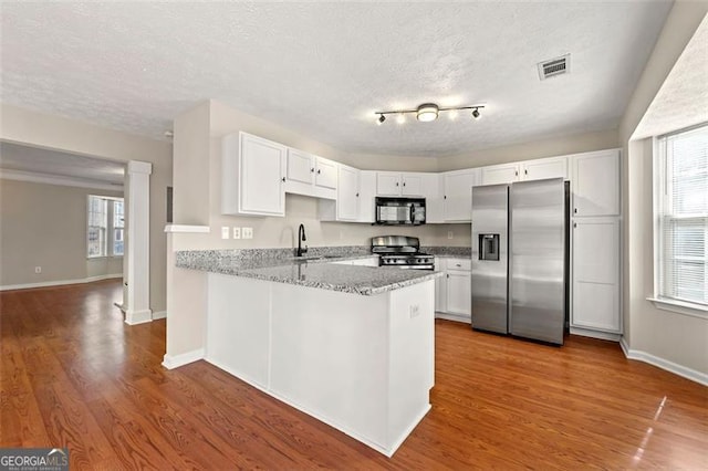 kitchen featuring stainless steel appliances, visible vents, white cabinets, a sink, and a peninsula