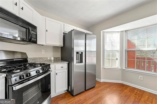 kitchen with baseboards, stainless steel appliances, a textured ceiling, light wood-type flooring, and white cabinetry