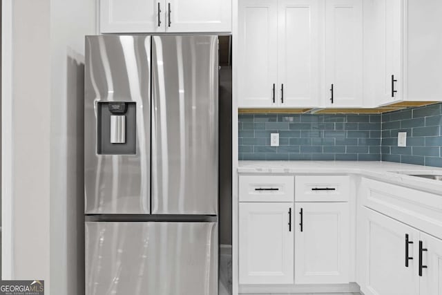 kitchen with light stone countertops, backsplash, white cabinetry, and stainless steel fridge with ice dispenser