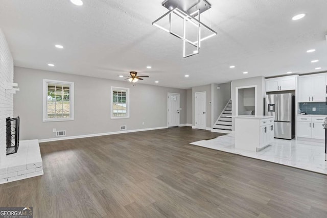 unfurnished living room featuring stairway, a brick fireplace, wood finished floors, and visible vents