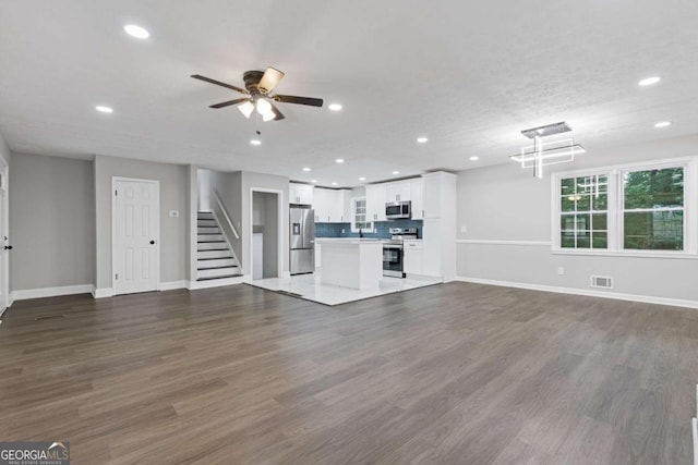 unfurnished living room with ceiling fan, stairway, and dark wood-type flooring