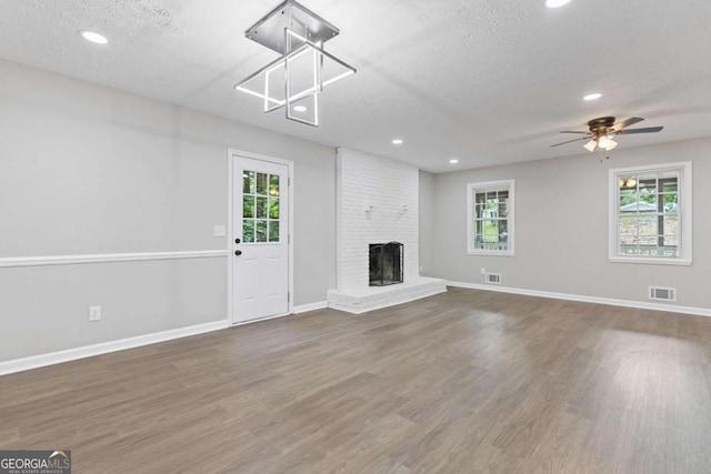 unfurnished living room featuring a textured ceiling, a brick fireplace, wood finished floors, and visible vents