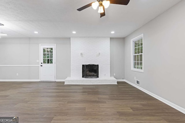 unfurnished living room with a brick fireplace, visible vents, baseboards, and wood finished floors