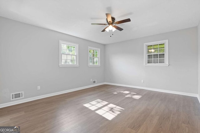 empty room with plenty of natural light, wood finished floors, visible vents, and baseboards