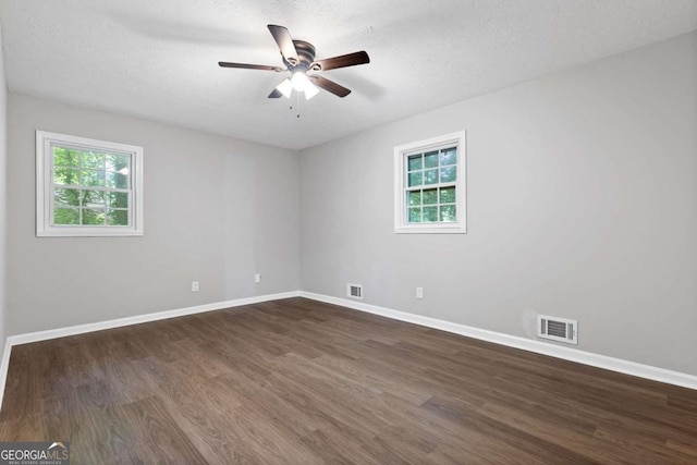 spare room with dark wood-style flooring, visible vents, and plenty of natural light