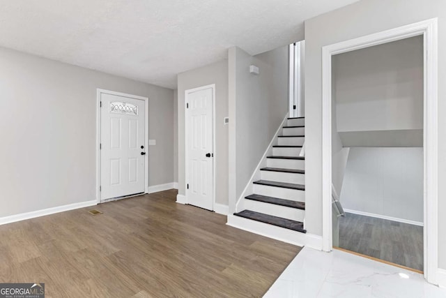 foyer entrance with stairway, a textured ceiling, baseboards, and wood finished floors