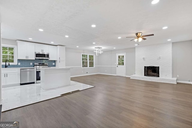 kitchen with stainless steel appliances, a fireplace, white cabinetry, light wood-type flooring, and decorative backsplash