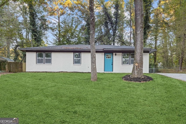 ranch-style home featuring brick siding, fence, and a front lawn