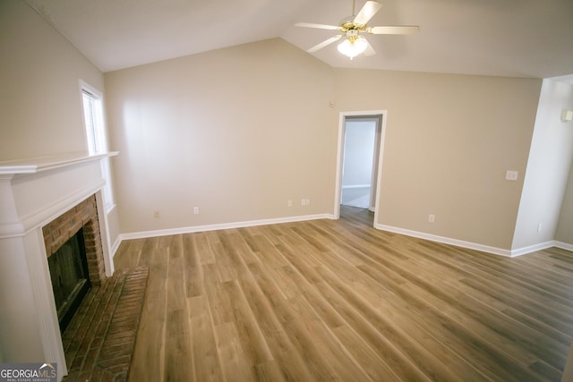 unfurnished living room with a ceiling fan, a brick fireplace, vaulted ceiling, wood finished floors, and baseboards