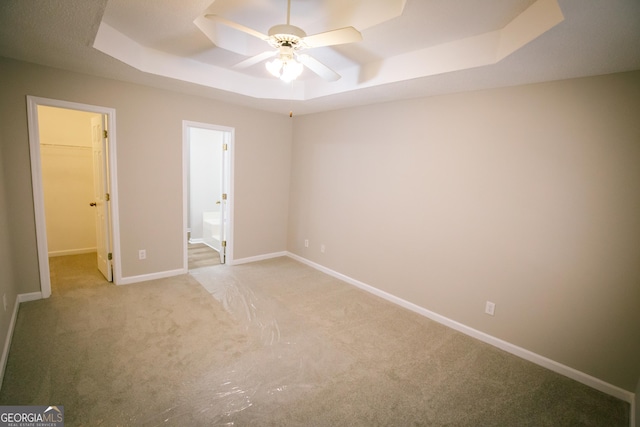 unfurnished bedroom with a raised ceiling, a spacious closet, ensuite bathroom, light carpet, and baseboards