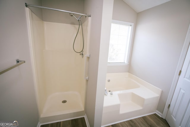 bathroom featuring a garden tub, wood finished floors, baseboards, vaulted ceiling, and a shower