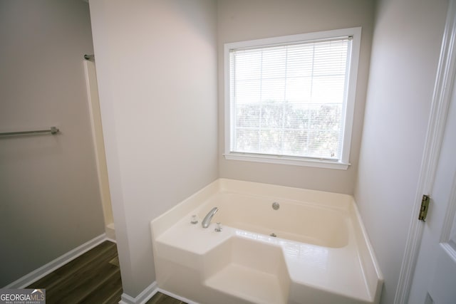 full bath with baseboards, a bath, and wood finished floors