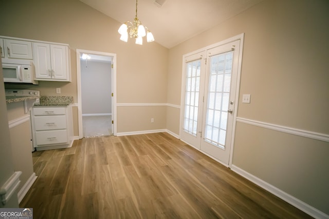 unfurnished dining area with light wood-type flooring, a notable chandelier, vaulted ceiling, and baseboards