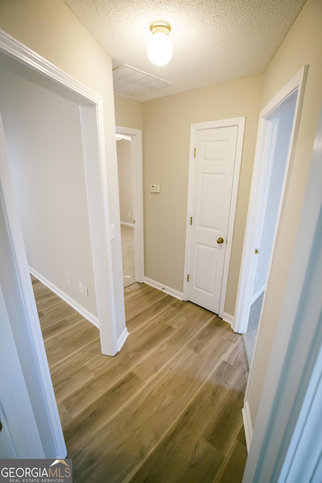 corridor with baseboards, light wood-style flooring, and a textured ceiling