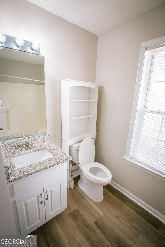 bathroom featuring toilet, a textured ceiling, vanity, wood finished floors, and baseboards