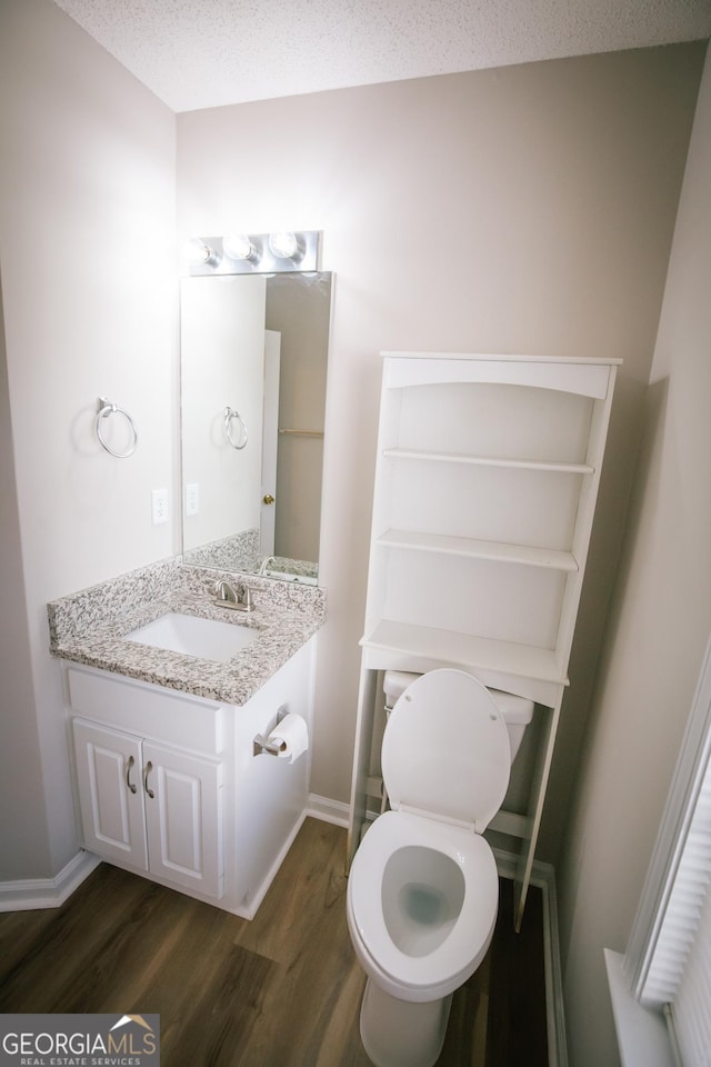 half bath with a textured ceiling, wood finished floors, vanity, and baseboards