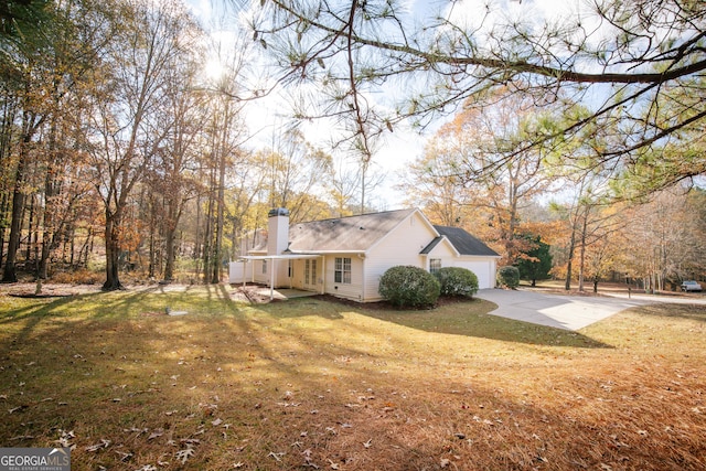 view of home's exterior featuring a yard, a chimney, an attached garage, and driveway