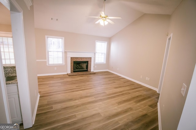 unfurnished living room featuring visible vents, a ceiling fan, lofted ceiling, light wood-type flooring, and a brick fireplace