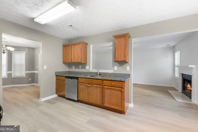 kitchen featuring brown cabinetry, a fireplace with flush hearth, light wood-style flooring, stainless steel dishwasher, and a sink