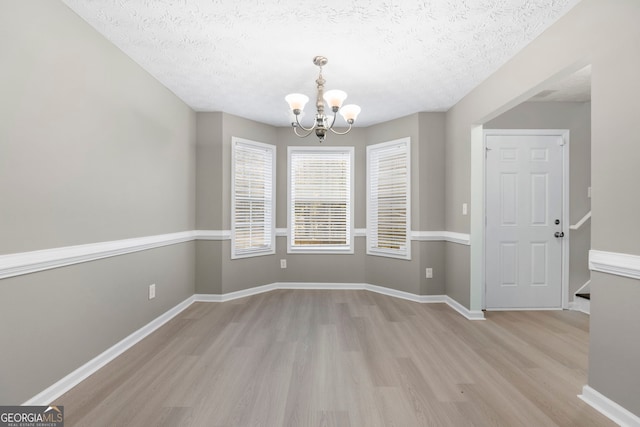 unfurnished dining area with a notable chandelier, a textured ceiling, baseboards, and wood finished floors