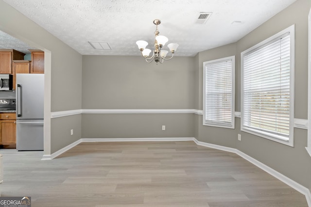 unfurnished dining area with a chandelier, light wood-type flooring, visible vents, and a textured ceiling