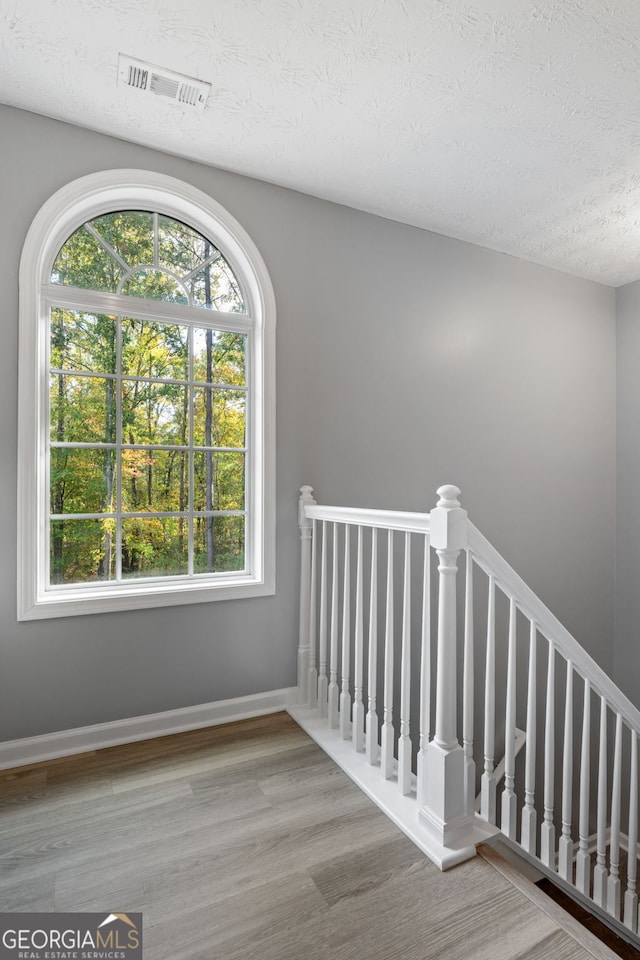 stairs featuring a textured ceiling, wood finished floors, visible vents, and baseboards