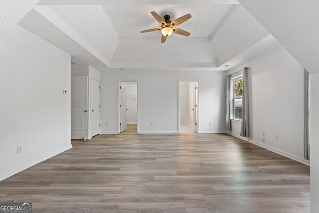 unfurnished bedroom featuring a tray ceiling, a spacious closet, baseboards, and wood finished floors