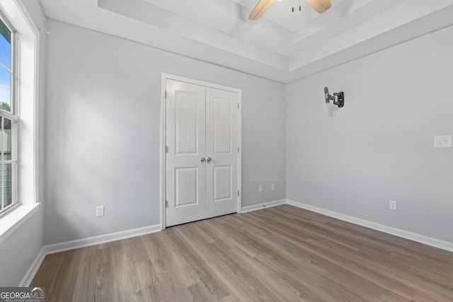 unfurnished bedroom featuring a tray ceiling, a closet, a ceiling fan, wood finished floors, and baseboards