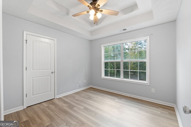 spare room featuring a ceiling fan, a raised ceiling, light wood-style flooring, and baseboards