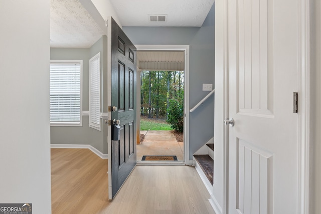 entryway with visible vents, a textured ceiling, baseboards, and wood finished floors