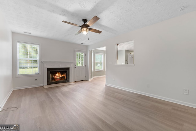 unfurnished living room featuring a wealth of natural light, light wood-type flooring, visible vents, and baseboards