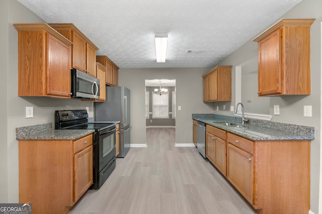 kitchen featuring stainless steel appliances, a sink, a textured ceiling, light wood-type flooring, and baseboards