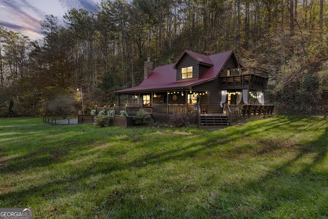 back of property featuring a chimney, a lawn, metal roof, a wooded view, and faux log siding