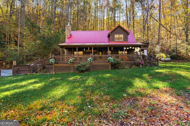 view of front of home with metal roof, a porch, a forest view, a front lawn, and a chimney