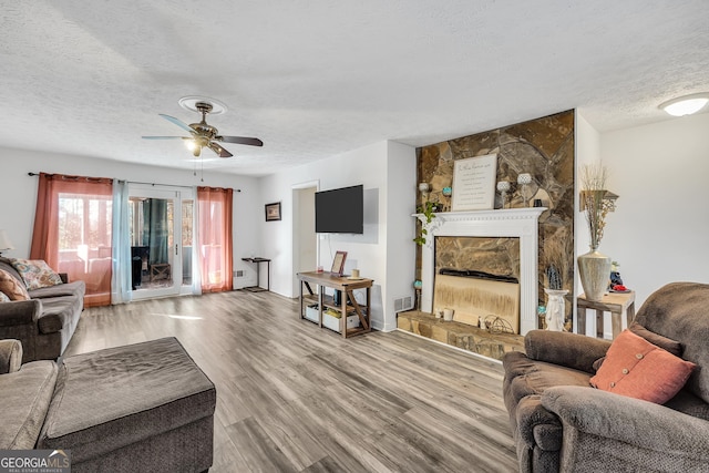 living room with a fireplace, visible vents, a ceiling fan, a textured ceiling, and wood finished floors