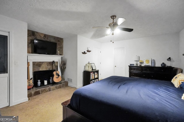 carpeted bedroom with a ceiling fan, a fireplace, visible vents, and a textured ceiling