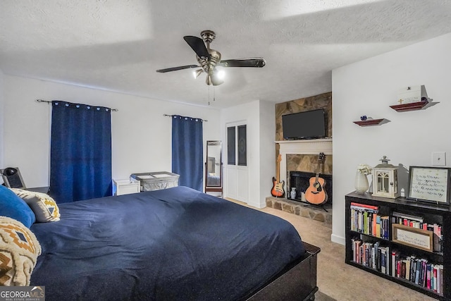 carpeted bedroom featuring a textured ceiling, ceiling fan, and a stone fireplace