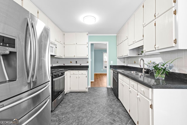 kitchen with stainless steel appliances, dark countertops, a sink, and white cabinets