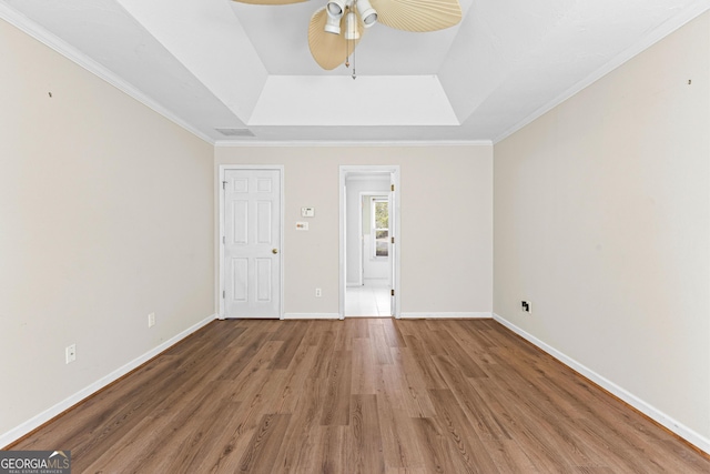 unfurnished bedroom with baseboards, ceiling fan, ornamental molding, wood finished floors, and a tray ceiling