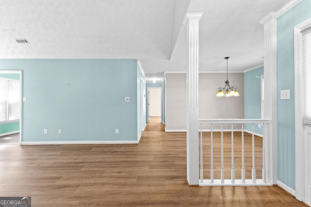 unfurnished room with a textured ceiling, wood finished floors, visible vents, an inviting chandelier, and ornate columns