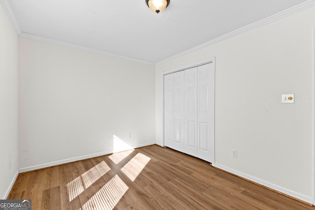 unfurnished bedroom with a closet, crown molding, baseboards, and wood finished floors