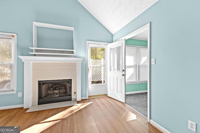 unfurnished living room with lofted ceiling, a fireplace with flush hearth, a textured ceiling, wood finished floors, and baseboards