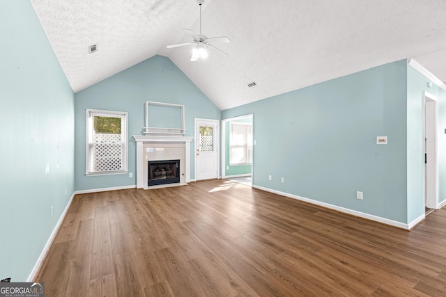 unfurnished living room featuring ceiling fan, a textured ceiling, a fireplace with flush hearth, wood finished floors, and baseboards