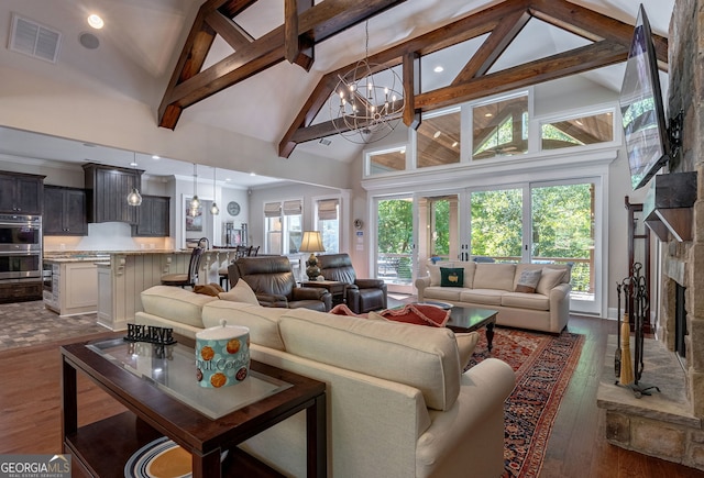 living area featuring plenty of natural light, visible vents, wood finished floors, a stone fireplace, and a chandelier