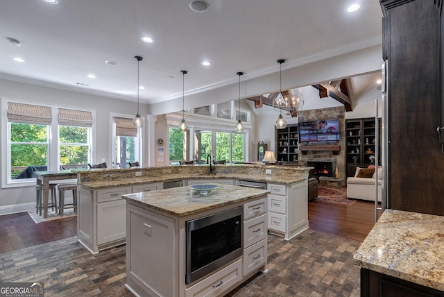 kitchen featuring a spacious island, built in microwave, ornamental molding, and a stone fireplace