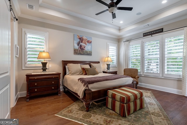 bedroom featuring baseboards, visible vents, a raised ceiling, wood finished floors, and crown molding