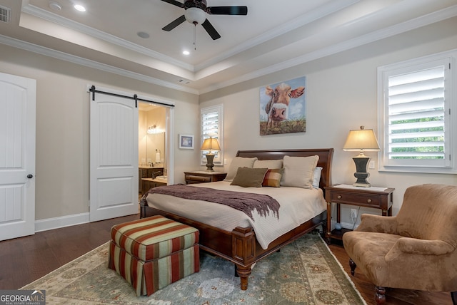 bedroom with a barn door, baseboards, visible vents, wood finished floors, and a tray ceiling