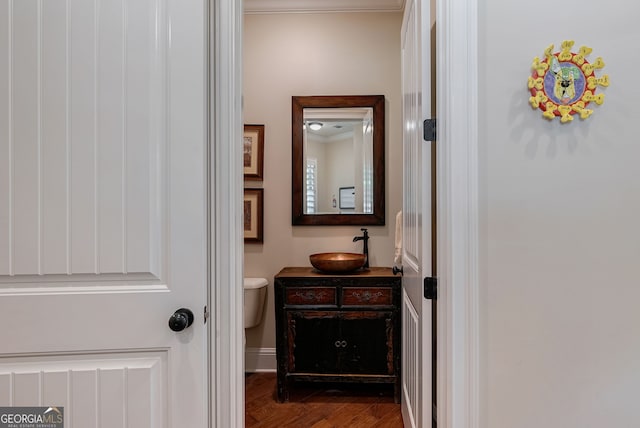 half bath featuring toilet, wood finished floors, vanity, baseboards, and crown molding